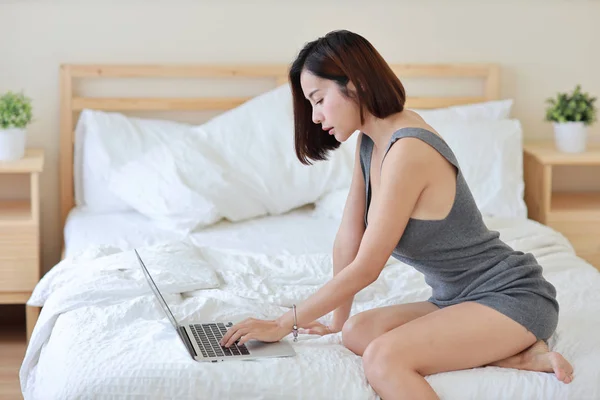 Zijaanzicht van volwassen freelance aziatische vrouw werken op computer en mobiele telefoon op bed in de slaapkamer — Stockfoto