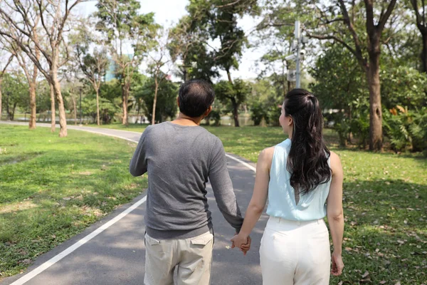 后视图中间成年亚洲夫妇步行和交谈在公园与自然绿树 — 图库照片