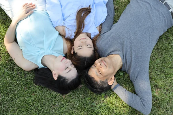 Su a testa in giù immagine di felice famiglia asiatica occhi di chiusura e felice volto sorridente mentre sdraiato sull'erba verde archiviato nella natura durante il periodo estivo — Foto Stock