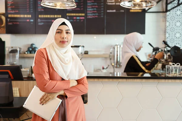 Junger muslimischer Angestellter Barista steht mit verschwommenem Hintergrund am Coffeeshop-Tresen und hält Tablet in der Hand — Stockfoto