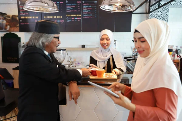 Cliente musulmano uomo d'affari indossa abito nero bere caffè al bancone con giovane musulmana barista sfondo donna d'affari — Foto Stock