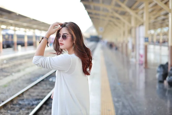 Vista posteriore ritratto di giovane donna asiatica in abito bianco con occhiali da sole in piedi e posa in stazione ferroviaria con sorriso e viso di bellezza — Foto Stock
