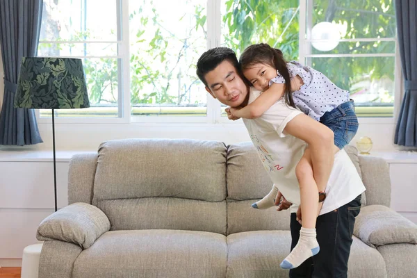 Szczęśliwy azjatycki tata trzyma swoją córkę, a on stoi w salonie z uśmiechniętą twarzą (koncepcja stylu życia) — Zdjęcie stockowe