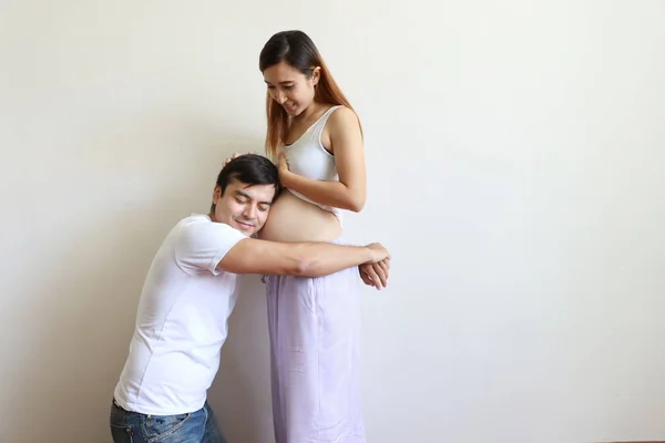 Jovem caucasiano marido abraçando jovem grávida asiático barriga esposa com fundo branco — Fotografia de Stock