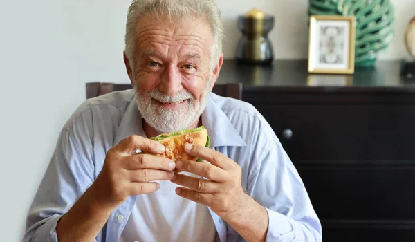 happy caucasian elderly eating hamburger in living room with smi