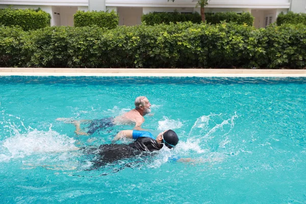 Vista lateral feliz anciano caucásico marido y anciano asiático esposa natación en piscina durante las vacaciones de jubilación con relajación en día soleado — Foto de Stock