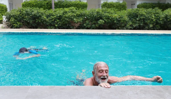 low angle view happy elderly caucasian husband and elderly asian wife swimming in pool during retirement holiday with relaxation on sunny day
