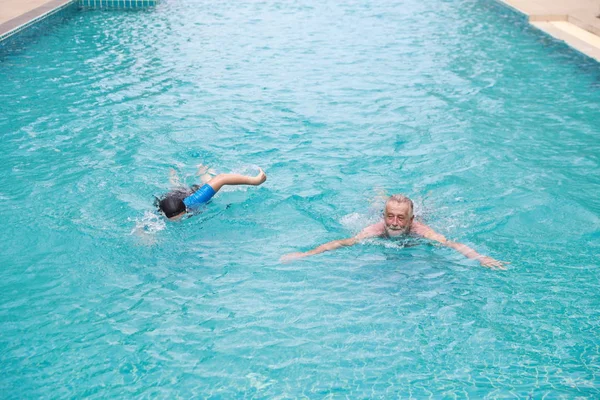 Feliz idosos caucasiano marido e idosos asiático esposa nadando na piscina durante a aposentadoria férias com relaxamento no dia ensolarado — Fotografia de Stock