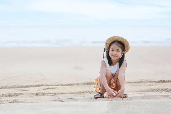 Szczęśliwy Asian Little Girl z miłym kapeluszem gry piasek na tropikalnej plaży z szczęśliwym uśmiechem — Zdjęcie stockowe