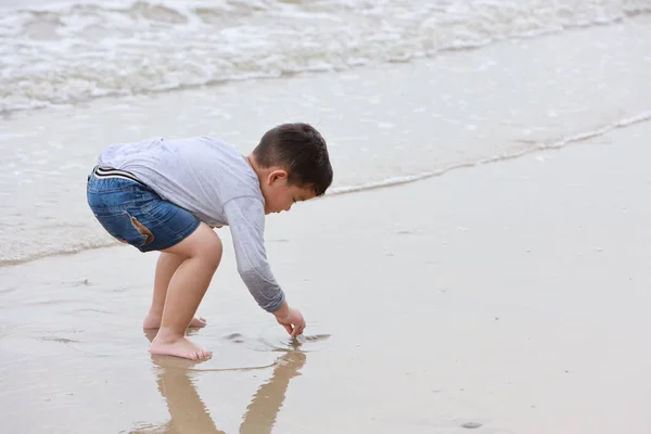 Lycklig asiatisk liten pojke som leker sand på tropisk strand med glatt leende ansikte på solig dag — Stockfoto