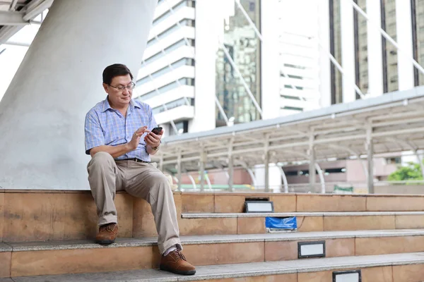asian traveler man in blue shirt with sitting on the stairs in downtown and using cell phone