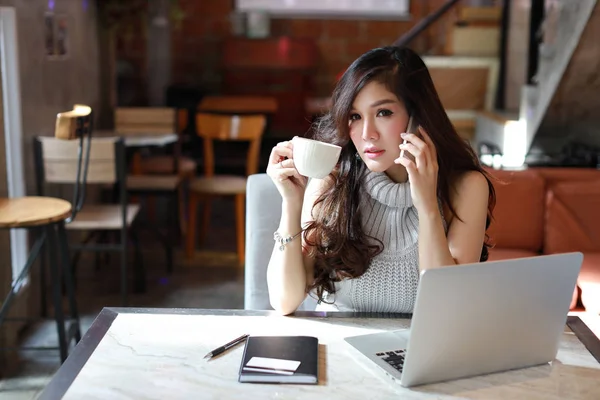 Belle et attrayante femme asiatique, cheveux longs en robe décontractée grise travaillant sur la table et buvant du café le matin tout en utilisant l'ordinateur dans un café — Photo