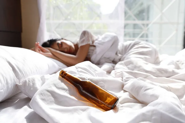 Ivre asiatique femme en blanc lingerie inconscient dans lit après boire trop d'alcool (se concentrer sur bouteille de liqueur ) — Photo