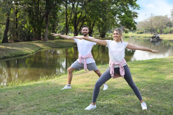 在夏天，年轻夫妇和健康的高加索人在公园里享受冥想或伸展在户外绿树下的瑜伽 — 图库照片