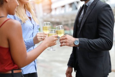 Başarılı çok ırklı iş adamları dışarıda kutlama yaparken gülümseyerek şampanya bardaklarını tokuşturuyor.