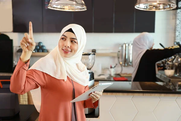 Giovane dipendente musulmano barista utilizzando tablet e indicando qualcosa al bancone della caffetteria con collega di lavoro sfondo sfocato — Foto Stock