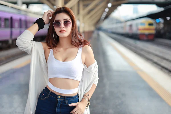 portrait of young asian woman in white dress with sun glassess standing and pose in train station with smiling and beauty face
