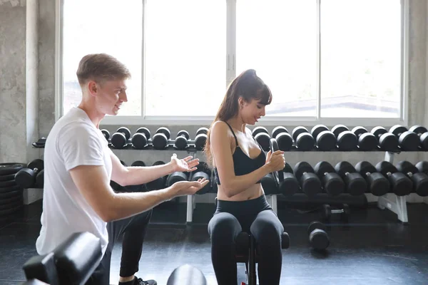 Sportovní kavkazský fitness žena zvedání činka v tělocvičně s kavkazský trenér muž — Stock fotografie