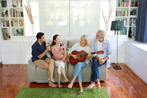 Happy Elder wieloetniczna rodzina siedzi i śpiewa piosenkę na szarej kanapie w salonie z uśmiechniętą twarzą — Zdjęcie stockowe