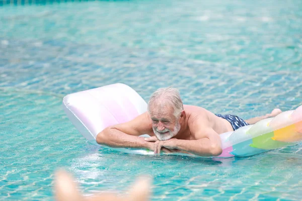 Feliz anciano caucásico nadar y jugar barco de goma en la piscina durante las vacaciones de jubilación con la relajación y la cara sonriente — Foto de Stock