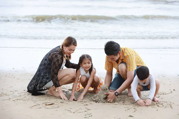 happy asian family father and mother playing with their children boy and girl, they playing and writing something on sandy beach during sunny day with laughing and smiling