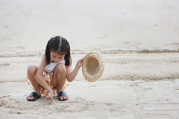 Felice asiatico poco asiatico ragazza con bello cappello giocare sabbia su sabbia spiaggia con felice sorridente faccia — Foto Stock