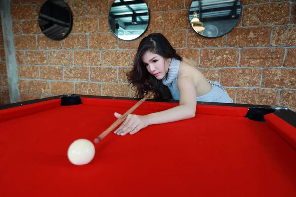 Genç ve güzel Asyalı bir kadın bilardo masasında bilardo oynuyor ve bilardo topuna nişan alıyor. — Stok fotoğraf