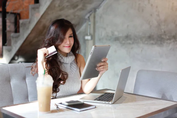 Gayri resmi kıyafet alışverişi yapan güzel Asyalı kadın ve tablet ve bilgisayardan online ödeme. Restoranda kredi kartını gösteriyor ve gülümseyerek kameraya bakıyor. — Stok fotoğraf