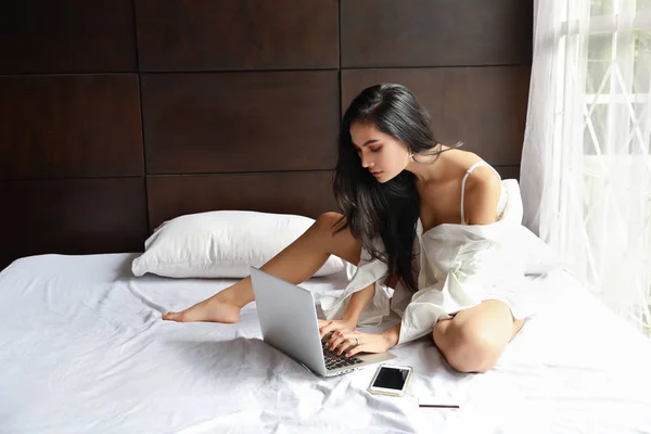 Adulte freelance asiatique femme en chemise blanche travaillant sur ordinateur et téléphone cellulaire dans chambre à coucher avec beauté visage — Photo