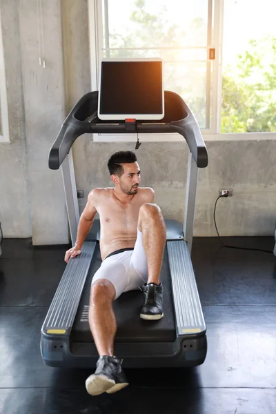 Спортивный кавказский мужчина в спортивной одежде, сидящий на беговой дорожке и отдыхающий от упражнений в тренажерном зале и отворачивающийся — стоковое фото
