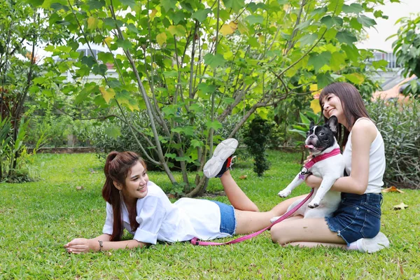 Красива дві молода азіатка в білій сорочці, яка лежить на траві і грає зі своїм милим собакою з щасливим і усміхненим обличчям в саду з зеленими деревами. (концепція дружби ) — стокове фото