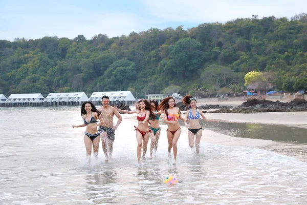 一群快乐而又性感的亚洲朋友，穿着比基尼和泳衣。他们在沙滩上跑步和踢足球。他们笑容满面，快乐无比. — 图库照片