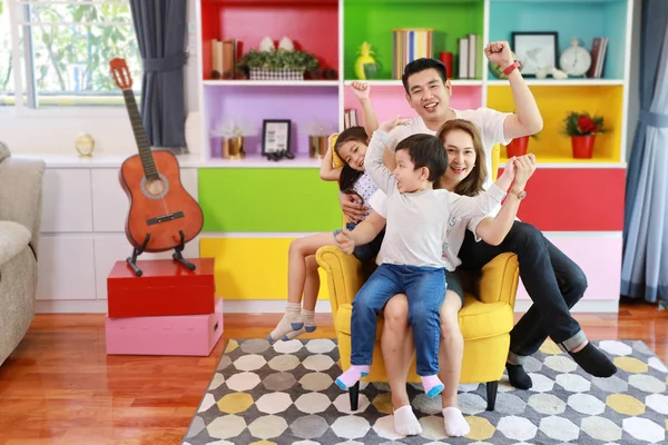 Szczęśliwy Azji rodzina ojciec, matka, syn i córka podnosząc ręce w górę z szczęśliwy uśmiechnięty twarz na szary sofa w salonie — Zdjęcie stockowe
