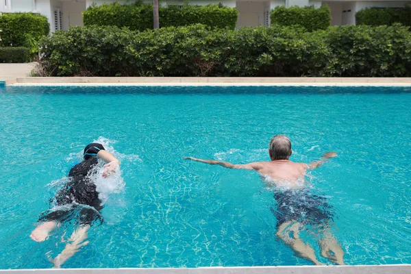 Feliz anciano caucásico marido y anciano asiático esposa nadando en piscina durante las vacaciones de jubilación con relajación y feliz en día soleado al aire libre —  Fotos de Stock
