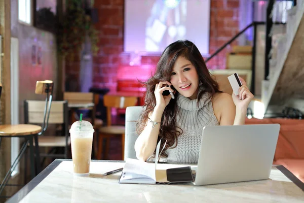 Güzel Asyalı bir kadın günlük kıyafet alışverişinde ve internette kredi kartını gösterirken ve kameraya gülümseyerek bakarken bilgisayardan ödeme yapıyor. — Stok fotoğraf