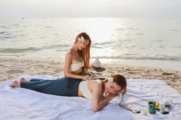 肩マッサージ 二人の若い美しくセクシーなアジアの女性の肖像画 夏休み中に砂浜に横たわっている間 白いドレスで長い髪はオイルスパマッサージサロンを楽しんで — ストック写真