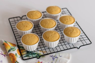 Beyaz bardaklarda, tel askıda vanilyalı kekler.