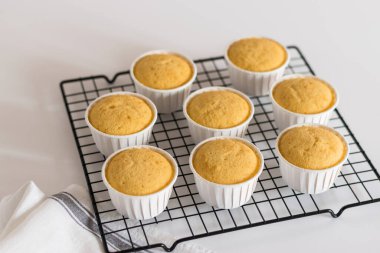 Beyaz bardaklarda, tel askıda vanilyalı kekler.