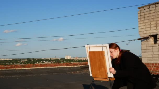红头发的女孩画了一幅画 在阳光明媚的日子里 在房子的屋顶上 — 图库视频影像