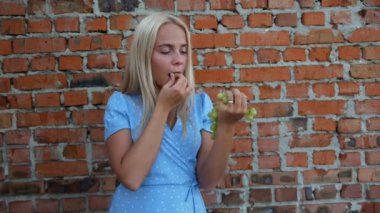 Mavi elbiseli kız üzüm, tuğla arka plan, mutluluk, gülümseme yiyor,