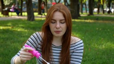 Kızıl saçlı kız parkta sabun kabarcıkları üfler O gülümseyen ve yaz ve mutluluk gülüyor 