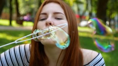 Kızıl saçlı kız parkta sabun kabarcıkları üfler O gülümseyen ve yaz ve mutluluk gülüyor 
