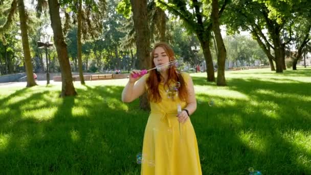 红头发的女孩在公园里吹肥皂泡 黄色的衣服她微笑着笑 夏天和幸福 — 图库视频影像