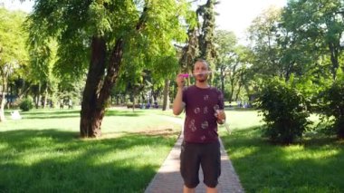 Sakallı adam sabun köpüğü üflüyor. Parkta güneşli bir gün