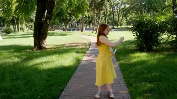 赤毛の女の子は公園で石鹸の泡を吹く 黄色のドレス彼女は微笑んで笑う 夏と幸せ — ストック動画