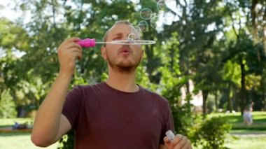 Sakallı adam sabun köpüğü üflüyor. Parkta güneşli bir gün