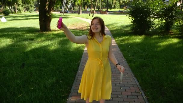 赤毛の女の子は公園で石鹸の泡を吹く 黄色のドレス彼女は微笑んで笑う 夏と幸せ — ストック動画