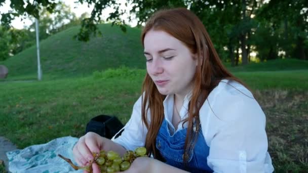 红发女孩在夏天在公园里吃水果 — 图库视频影像