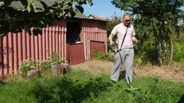 Pembe tişörtlü bir adam elektrikli tırpanla çimleri biçer.