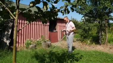Pembe tişörtlü bir adam elektrikli tırpanla çimleri biçer.
